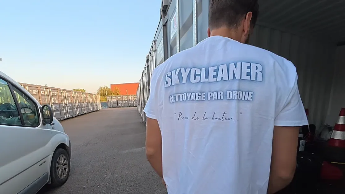 Technicien Skycleaner de dos en tee-shirt « nettoyage par drone », devant le véhicule d'intervention